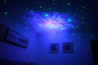 Colorful nebula-like projection of blue, purple and pink lights with scattered green stars on a ceiling.