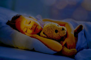 A sleeping child cuddling with a teddy bear under blue covers.